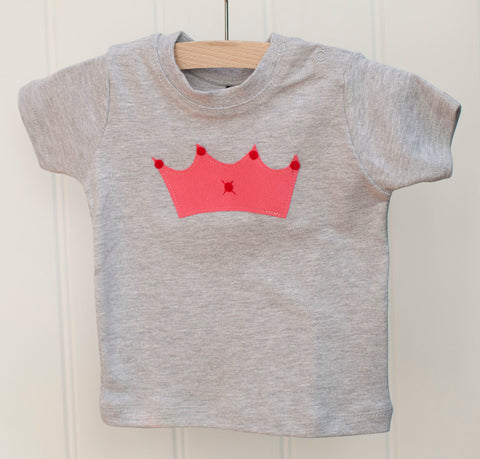 Grey melange baby t-shirt featuring a pink crown design with red details. T-shirt has poppers on the shoulder for easy wear. T-shirt hangs against a white panneled background. - isabee.co.uk