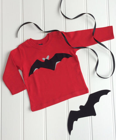 Red, long-sleeved baby t-shirt featuring a black bat design with reflective details. T-shirt is displayed on a white panneled background with a black bat and a black ribbon beside it. - isabee.co.uk