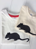 Two folded organic cotton t-shirts with a hand applique mouse on the front. The top t-shirt for babies is natural white, the bottom t-shirt for children is  cream. The mouse is made of fine stripe grey cotton melange, with black eye, ears and tail. Designed and hand made in the Isabee London studio. Available in four sizes for babies (3 -24 months). Includes Isabee easy-wear neck with poppers. Also available for ages 2 to 5 years.