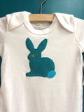 Close up photo of white organic cotton sleepsuit for babies with hand applique rabbit sitting on the front in fine stripe teal with teal blue tail and lime eye detail. Available in two sizes 0-3 and 3-6 months, ideal for newborn and premature babies. Handmade in London - isabee.co.uk