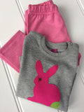 Baby Rabbit soft grey long-sleeved t-shirt featuring a hand-applique rabbit in fuschia pink, with leaf green tail and eye detail. The long-sleeved t-shirt has shoulder poppers on one side and the top is folded and resting on a pair of soft cotton jersey leggings for babies, the leggings are fine-stripe pink (candy and soft pink) and have an elasticated waist. Made in London by Isabee.