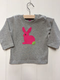 Baby Rabbit long-sleeved t-shirt on a hanger.  The top is a soft grey colour and  features an applique rabbit in fuschia pink with a leaf green tail and eye detail. Shoulder poppers on one side for easy wear. Hand made by Isabee in London.