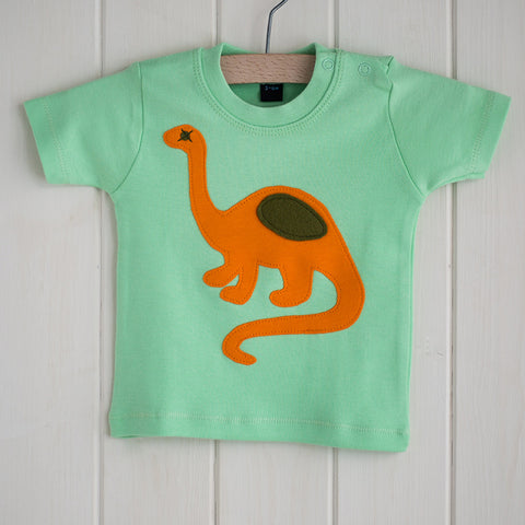 Baby Dinosaur T-shirt - mint-green t-shirt featuring an orange dinosaur with olive details. T-shirt has two poppers on the shoulder. It is displayed in a hanger in front of a white panelled background. - isabee.co.uk
