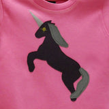 Close-up of a bubblegum pink baby's t-shirt featuring an augergine coloured appliquéd Unicorn design with a reflective horn and an olive green mane and tail. Unicorn is rearing on its hind legs. - isabee.co.uk