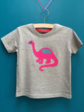 Children's light grey melange t-shirt featuring an appliquéd pink dinosaur with blue details. Dinosaur is reaching its long neck up and the tail is curved around beside. Displayed on a teal background. - isabee.co.uk